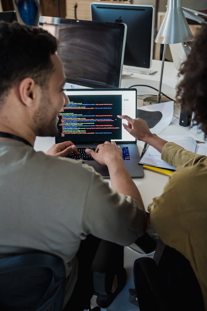 who-we-are Two programmers working together on a laptop, discussing code in a modern office setting.